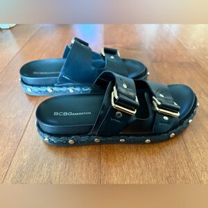 BCBGeneration 7.5 black sandals with gold buckles and studded sides